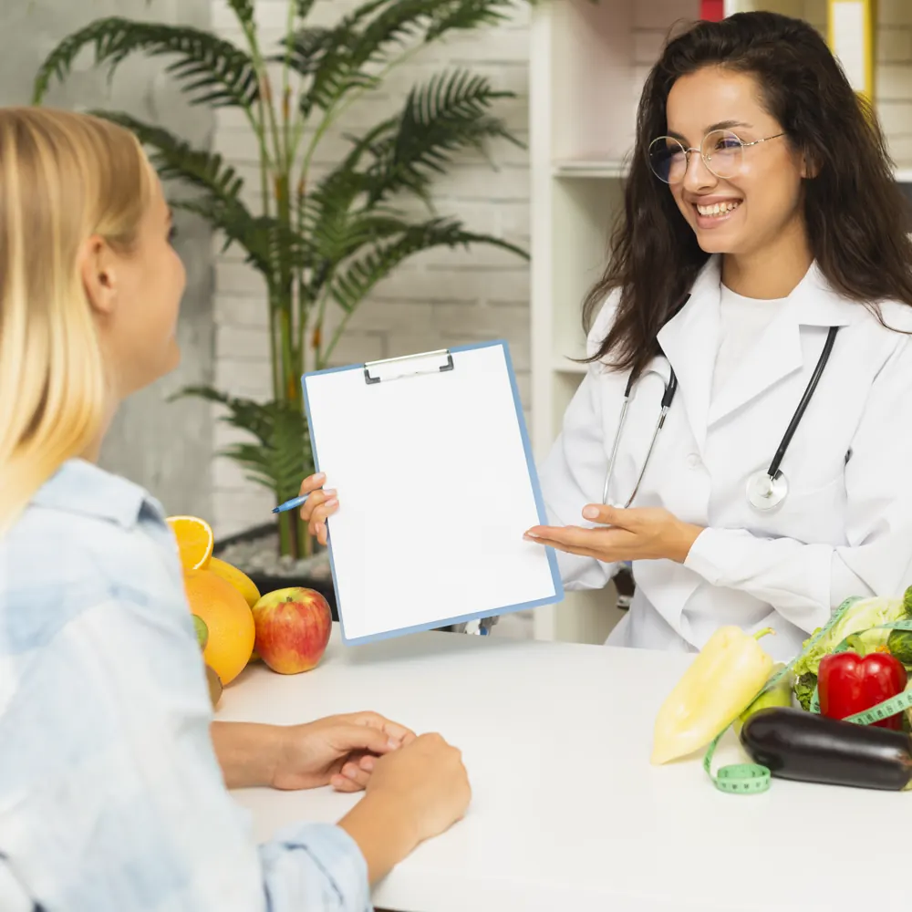 Nutrióloga explicando un plan de alimentación a una paciente, con verduras y fruta sobre el escritorio