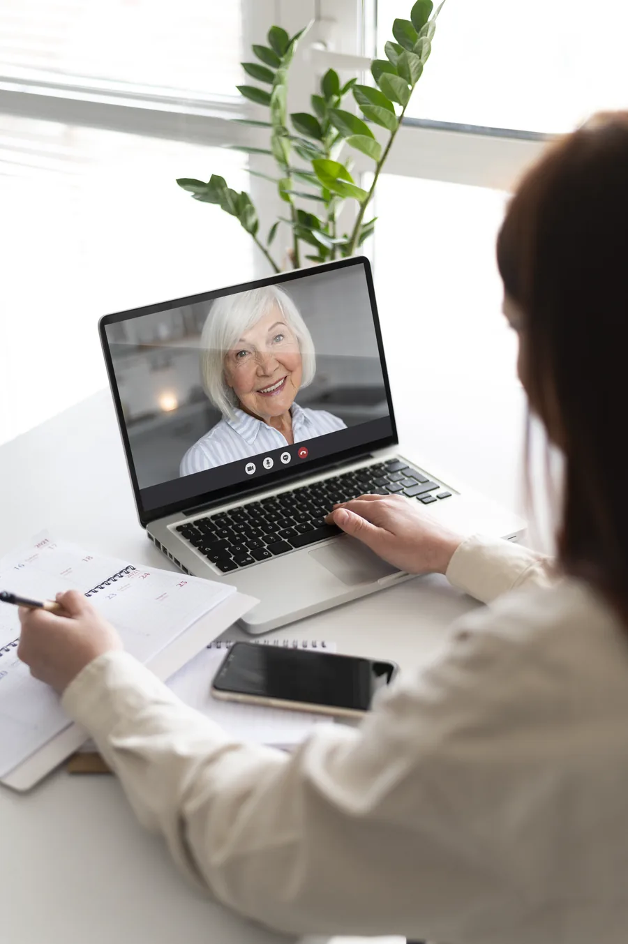 Paciente en videollamada de consulta en línea, tomando notas frente a su computadora
